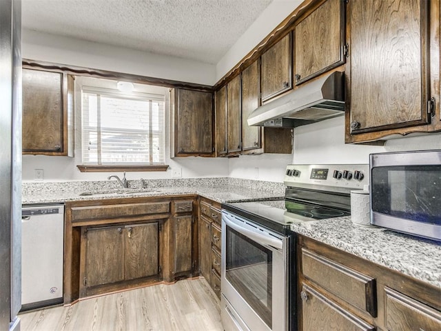 kitchen featuring under cabinet range hood, stainless steel appliances, a sink, light wood-style flooring, and a textured ceiling