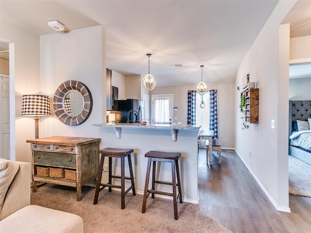 11704 NW 99th Ter, Yukon, OK 73099 - kitchen with a kitchen bar, light stone counters, a peninsula, decorative light fixtures, and black refrigerator with ice dispenser