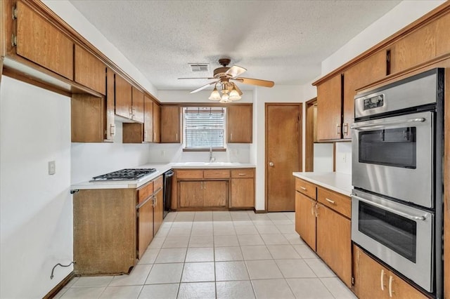 708 Cross Timbers Dr, Moore, OK 73160 - kitchen with appliances with stainless steel finishes, brown cabinetry, a sink, a textured ceiling, and ceiling fan