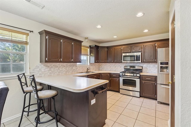 316 SE 6th St, Moore, OK 73160 - kitchen featuring stainless steel appliances, backsplash, dark brown cabinets, a peninsula, and a kitchen breakfast bar