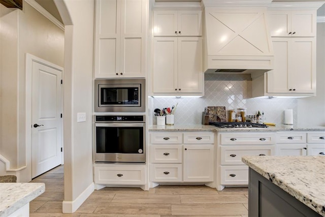12004 SW 49th St, Mustang, OK 73064 - kitchen featuring appliances with stainless steel finishes, light wood-style flooring, custom range hood, and tasteful backsplash