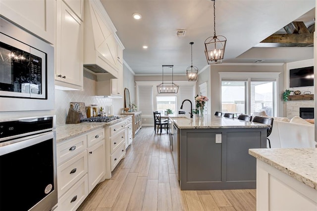 12004 SW 49th St, Mustang, OK 73064 - kitchen featuring appliances with stainless steel finishes, a kitchen island with sink, open floor plan, white cabinetry, and custom exhaust hood