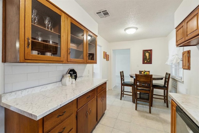 3831 NW Bell Ave, Lawton, OK 73505 - kitchen featuring stainless steel dishwasher, backsplash, a textured ceiling, brown cabinetry, and glass insert cabinets