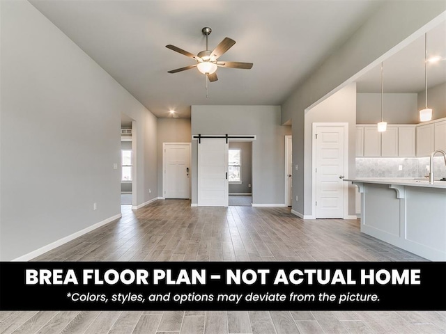1100 Redwood Creek Dr, Yukon, OK 73099 - unfurnished living room featuring a barn door, light wood-type flooring, ceiling fan, baseboards, and a sink