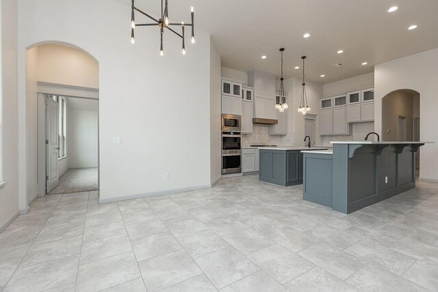 9120 SW 34th St, Oklahoma City, OK 73179 - kitchen featuring appliances with stainless steel finishes, a kitchen island with sink, arched walkways, light countertops, and recessed lighting