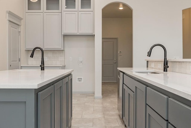 9120 SW 34th St, Oklahoma City, OK 73179 - kitchen featuring gray cabinets, a sink, arched walkways, decorative backsplash, and glass insert cabinets