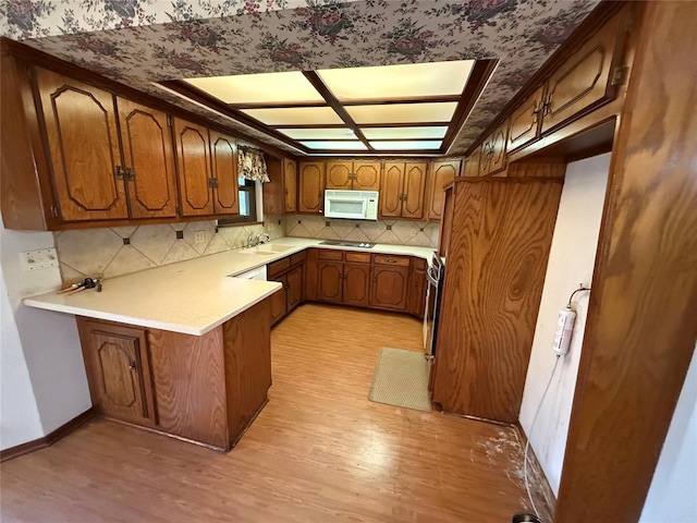 5624 N Mueller Ave, Bethany, OK 73008 - kitchen with white microwave, a peninsula, light wood-type flooring, brown cabinetry, and tasteful backsplash