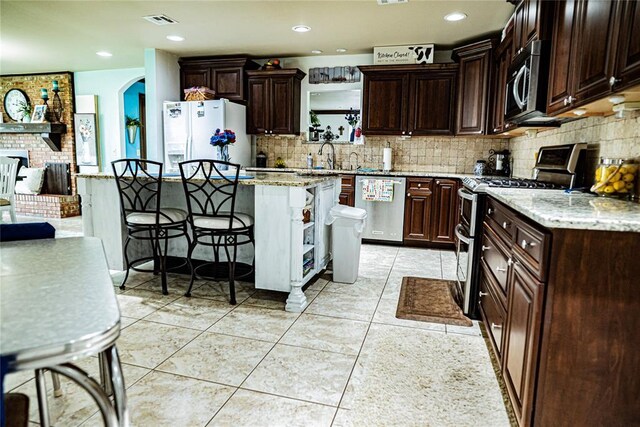 8100 N Burns Rd, Edmond, OK 73025 - kitchen with stainless steel appliances, a breakfast bar, backsplash, a center island, and dark brown cabinetry