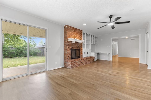 6 Utah Ave, Yukon, OK 73099 - unfurnished living room with a ceiling fan, light wood-style floors, baseboards, a brick fireplace, and a textured ceiling