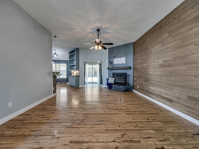1900 New Haven Ct, Moore, OK 73160 - unfurnished living room with a ceiling fan, a fireplace, wood finished floors, baseboards, and wood walls