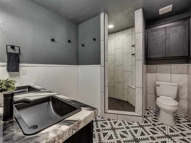 1900 New Haven Ct, Moore, OK 73160 - bathroom featuring toilet, tiled shower, tile patterned flooring, a wainscoted wall, and a textured ceiling