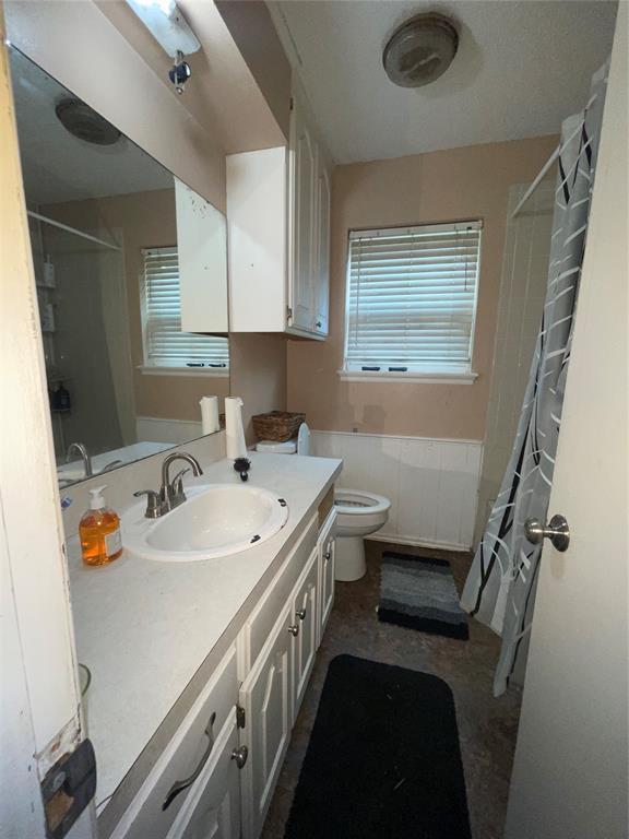 617 Mark Dr, Oklahoma City, OK 73115 - bathroom with vanity, curtained shower, toilet, and a wainscoted wall