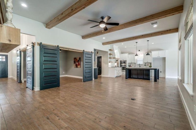 600 NW 186th St, Edmond, OK 73012 - unfurnished living room with a barn door, ceiling fan, baseboards, wood finished floors, and beamed ceiling