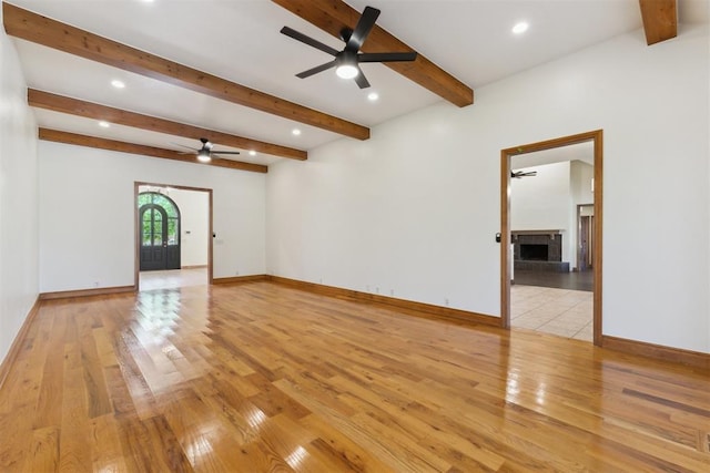 18617 Wolf Creek Dr, Edmond, OK 73012 - empty room featuring a ceiling fan, light wood-style flooring, a fireplace with raised hearth, beamed ceiling, and baseboards