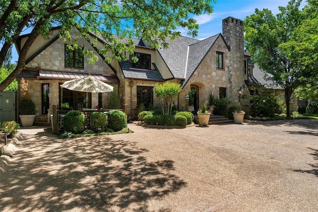 6638 Avondale Dr, Nichols Hills, OK 73116 - tudor-style house featuring stone siding, a chimney, and a standing seam roof