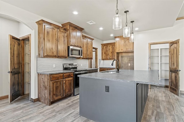 2414 Black Jack Way, Blanchard, OK 73010 - kitchen featuring stainless steel appliances, a sink, light wood-type flooring, backsplash, and a center island with sink