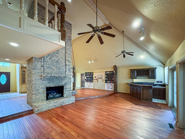 2010 Saddleback Blvd, Norman, OK 73072 - unfurnished living room featuring a fireplace, a ceiling fan, light wood-style floors, high vaulted ceiling, and a textured ceiling
