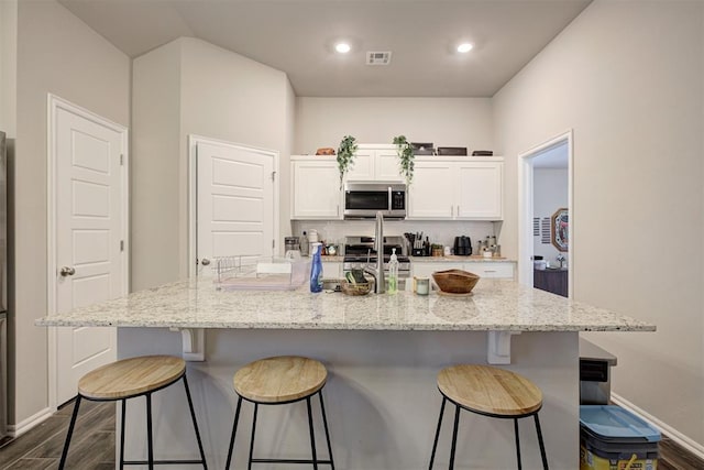 1301 Harvest Trl, Yukon, OK 73099 - kitchen with stainless steel appliances, white cabinetry, dark wood finished floors, a breakfast bar, and a kitchen island with sink