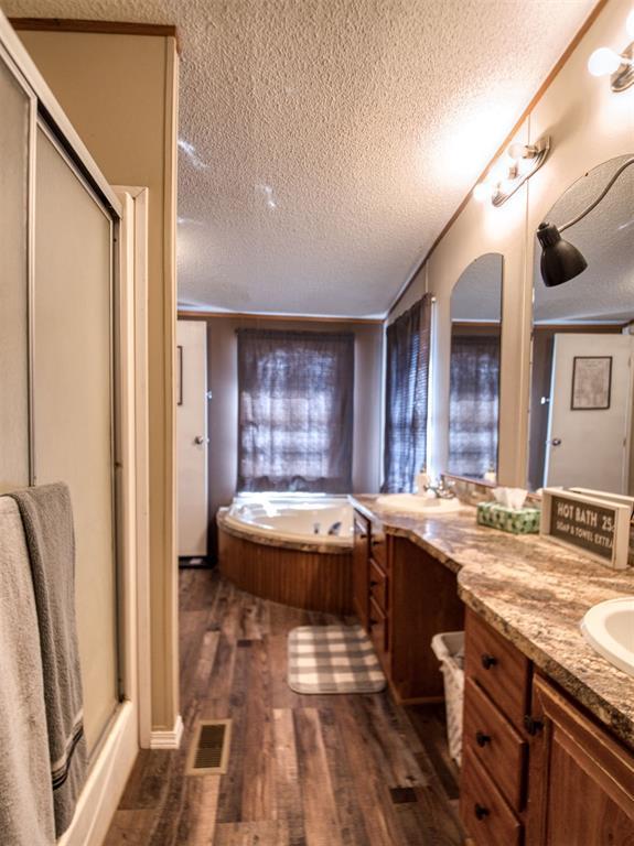 15026 N County Road 3370th Rd, Stratford, OK 74872 - full bathroom featuring a textured ceiling, wood finished floors, vanity, a stall shower, and a garden tub