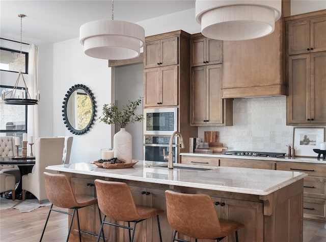9117 SW 90th St, Mustang, OK 73064 - kitchen featuring a sink, appliances with stainless steel finishes, tasteful backsplash, light wood-type flooring, and a kitchen island with sink