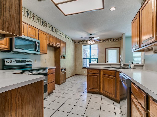 2601 Northwood Ln, Edmond, OK 73013 - kitchen featuring appliances with stainless steel finishes, brown cabinets, light countertops, plenty of natural light, and a textured ceiling