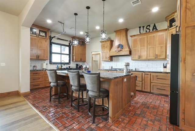 9027 Ns 3500th Rd, Prague, OK 74864 - kitchen featuring custom range hood, a kitchen island, a breakfast bar area, tasteful backsplash, and brick floors