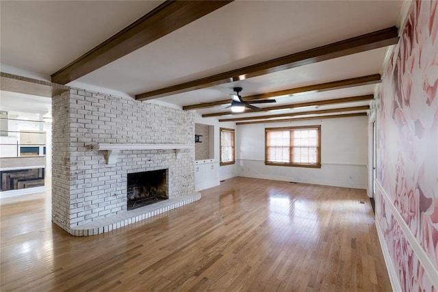 1301 W C Ave, Elk City, OK 73644 - unfurnished living room with ceiling fan, a fireplace, wood finished floors, and beamed ceiling