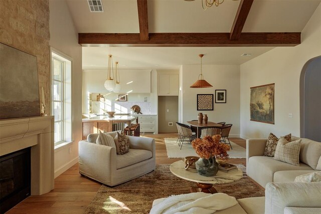 3817 Shady Hill Trl, Edmond, OK 73034 - living room featuring light wood-type flooring, beam ceiling, arched walkways, a glass covered fireplace, and baseboards