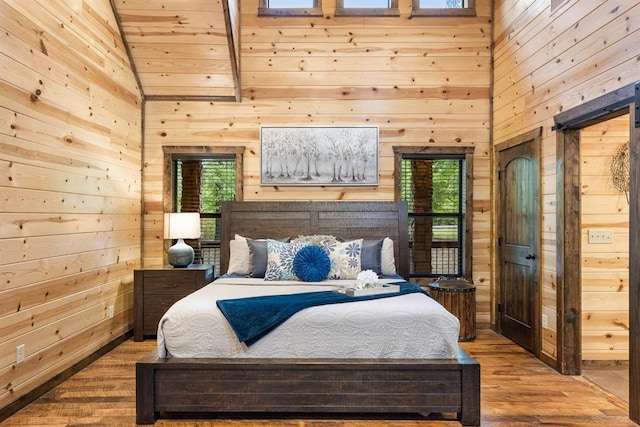 186 W Eagle Mountain Trl, Broken Bow, OK 74728 - bedroom with wood walls, wood finished floors, multiple windows, high vaulted ceiling, and a barn door