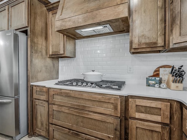 11052 NW 21st St, Yukon, OK 73099 - kitchen featuring stainless steel appliances, decorative backsplash, light countertops, ventilation hood, and brown cabinets