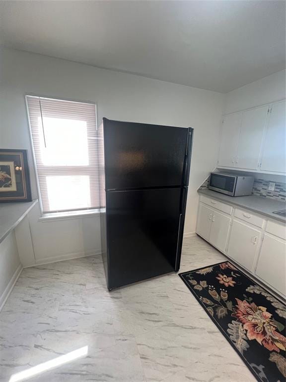 414 N 1st St, Tecumseh, OK 74873 - kitchen with freestanding refrigerator, stainless steel microwave, light marble finish floors, white cabinets, and light countertops