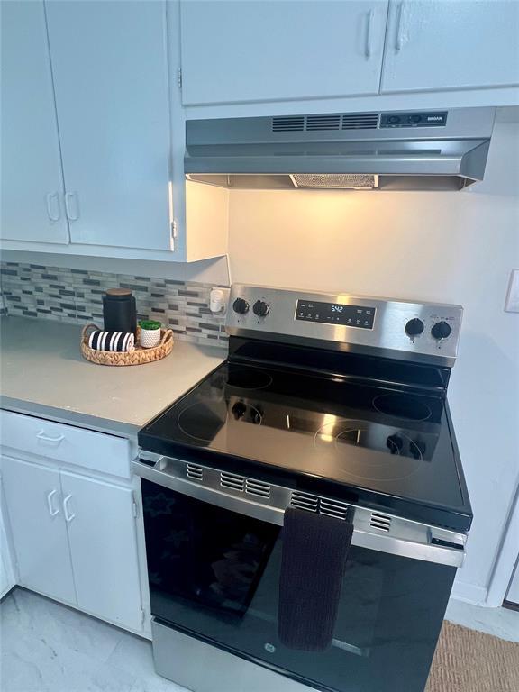 414 N 1st St, Tecumseh, OK 74873 - kitchen featuring stainless steel electric range, under cabinet range hood, light countertops, decorative backsplash, and white cabinetry