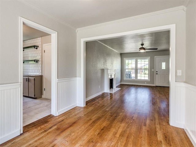 2748 Lancaster Ln, Oklahoma City, OK 73116 - unfurnished living room featuring ceiling fan, wood finished floors, crown molding, a wainscoted wall, and a fireplace