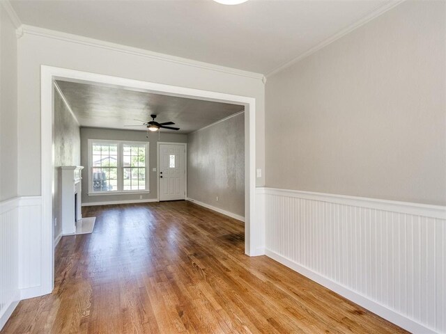 2748 Lancaster Ln, Oklahoma City, OK 73116 - spare room featuring wood finished floors, ceiling fan, a fireplace, crown molding, and a wainscoted wall