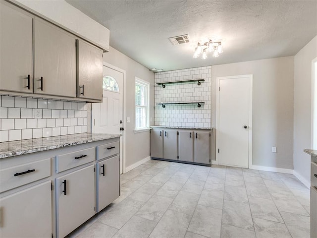 2748 Lancaster Ln, Oklahoma City, OK 73116 - kitchen featuring backsplash, baseboards, a textured ceiling, and light stone counters