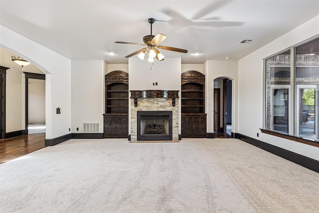 3101 Monica Ln, Moore, OK 73160 - unfurnished living room featuring arched walkways, carpet flooring, a ceiling fan, a fireplace, and built in shelves