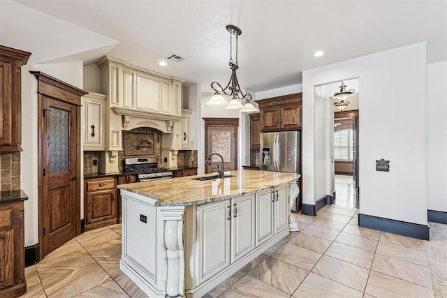 3101 Monica Ln, Moore, OK 73160 - kitchen featuring appliances with stainless steel finishes, cream cabinetry, backsplash, light stone countertops, and decorative light fixtures