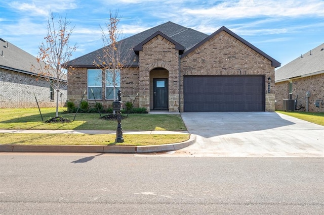 2836 NW 28th St, Yukon, OK 73099 - french country style house featuring brick siding, an attached garage, concrete driveway, a front yard, and a shingled roof