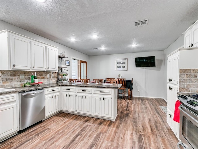 1202 N 8th Ave, Purcell, OK 73080 - kitchen featuring stainless steel appliances, a peninsula, light wood-style flooring, white cabinets, and a textured ceiling