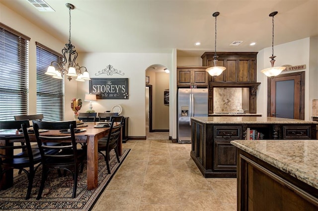 2139 Rivanna Way, Edmond, OK 73034 - kitchen with stainless steel fridge with ice dispenser, arched walkways, hanging light fixtures, light stone countertops, and dark brown cabinets