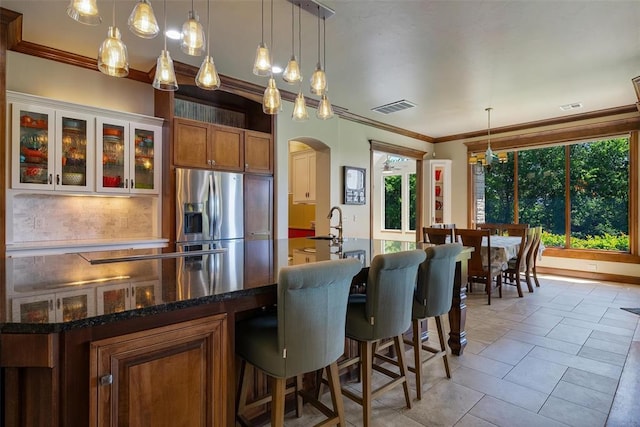 1516 Brook Bank Dr, Jones, OK 73049 - kitchen featuring stainless steel fridge with ice dispenser, arched walkways, brown cabinets, crown molding, and a breakfast bar area