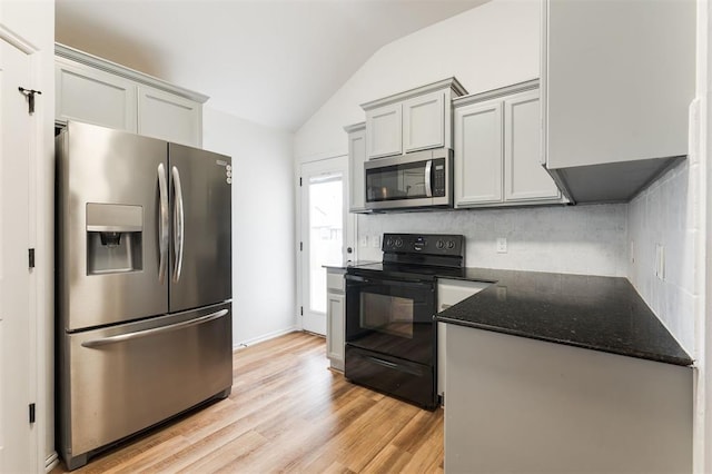 2304 NW 196th Ter, Edmond, OK 73012 - kitchen with stainless steel appliances, lofted ceiling, light wood-type flooring, gray cabinetry, and dark stone countertops