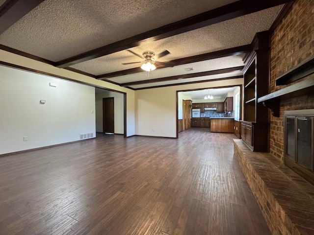 19 Mohican Cir, Shawnee, OK 74801 - unfurnished living room featuring a textured ceiling, a brick fireplace, baseboards, dark wood finished floors, and beam ceiling