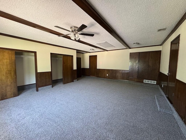 19 Mohican Cir, Shawnee, OK 74801 - unfurnished bedroom with a textured ceiling, wooden walls, wainscoting, two closets, and ceiling fan