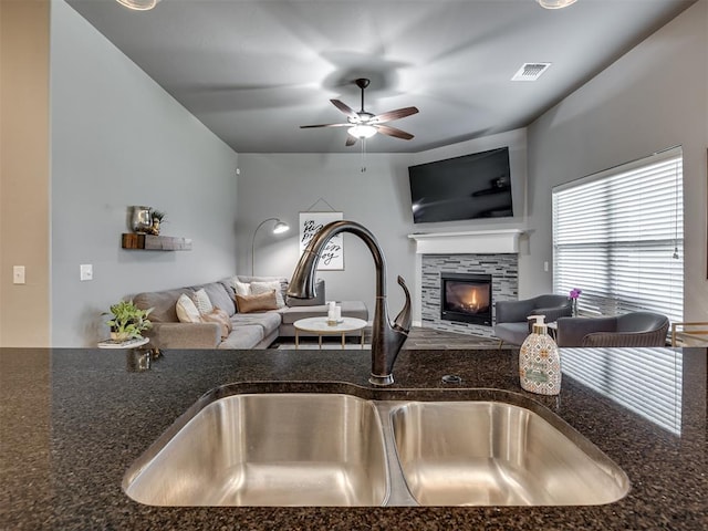 8109 NW 160th Ter, Edmond, OK 73013 - kitchen with open floor plan, a sink, ceiling fan, a fireplace, and dark stone countertops