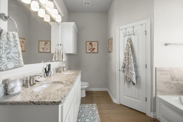 3409 Ontario Cir, Oklahoma City, OK 73160 - bathroom featuring double vanity, toilet, a garden tub, wood finished floors, and baseboards