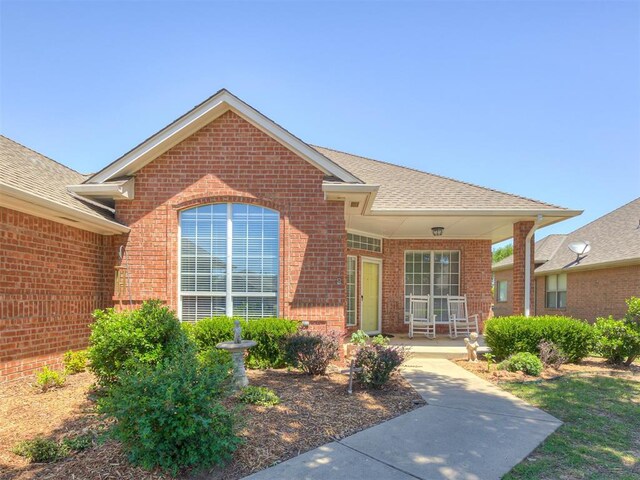 8413 NW 64th Ter, Oklahoma City, OK 73132 - view of exterior entry featuring brick siding, a porch, and a shingled roof