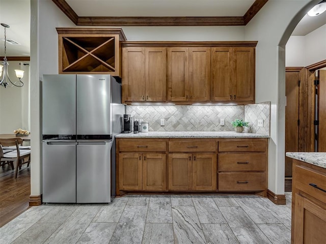18854 Marbella Ln, Harrah, OK 73045 - kitchen with freestanding refrigerator, crown molding, brown cabinetry, arched walkways, and light stone counters