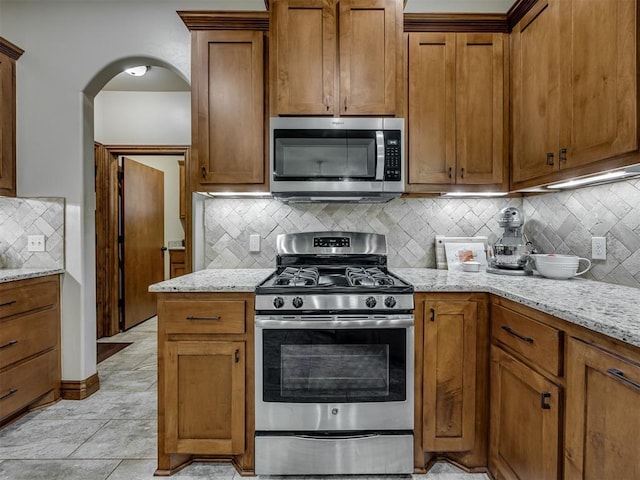 18854 Marbella Ln, Harrah, OK 73045 - kitchen featuring stainless steel appliances, decorative backsplash, light stone counters, and brown cabinets