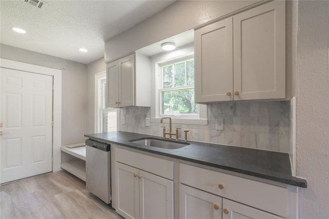 2301 N Kelham Ave, Oklahoma City, OK 73111 - kitchen featuring stainless steel dishwasher, a sink, tasteful backsplash, light wood-style flooring, and a textured ceiling